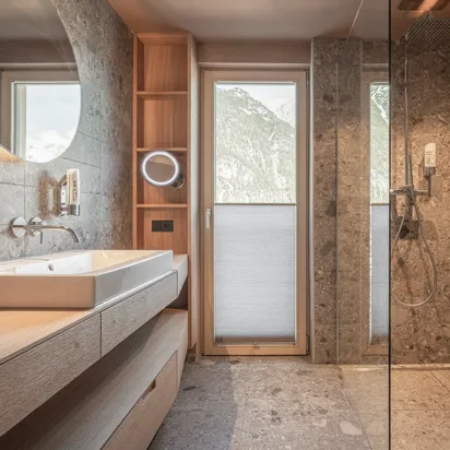 Modern bathroom with stone tiles, walk-in rain shower and wooden vanity with large mirror